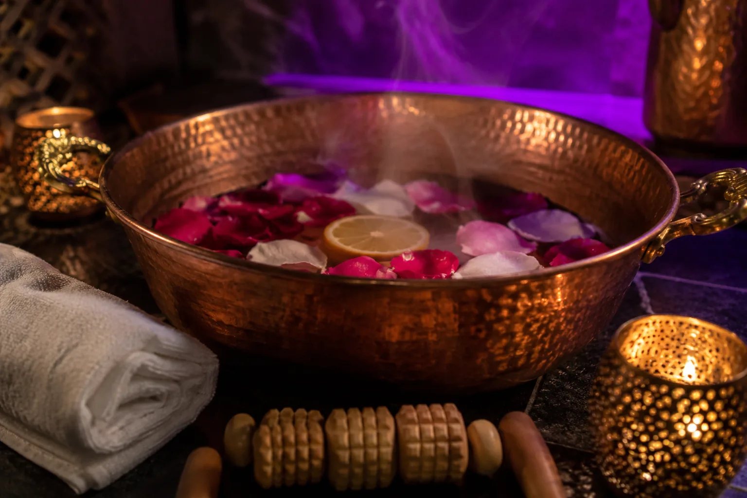 Copper basin for foot care with rose petals and a wooden roller